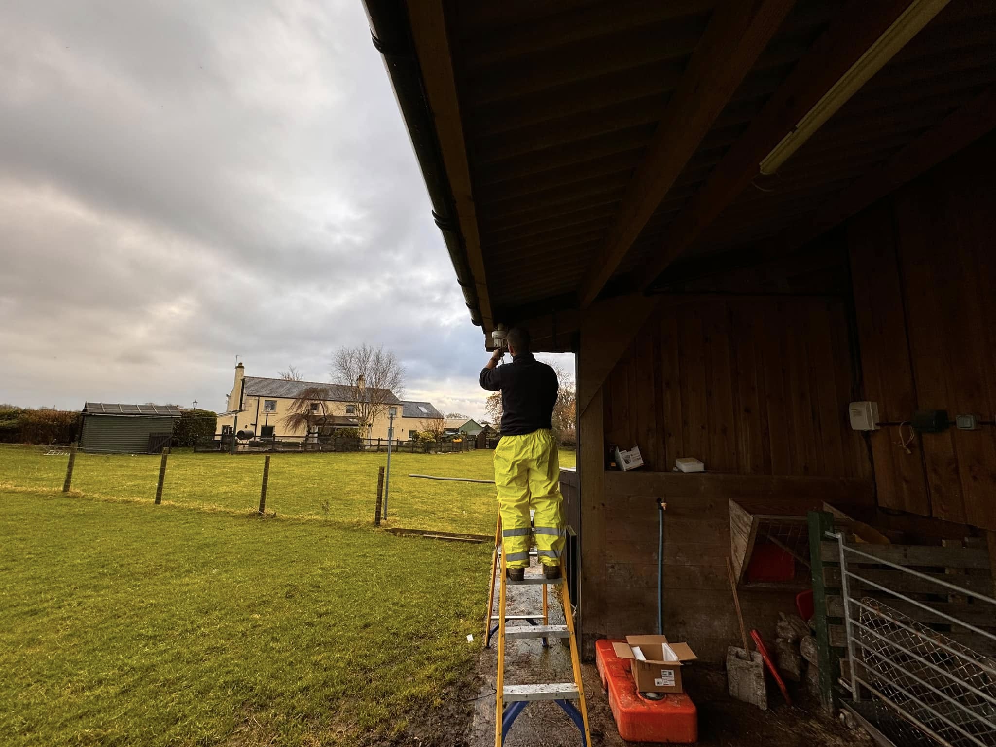 Matrix FSE engineer installing a CCTV camera on a lambing shed with farmhouse visible in background, Preston