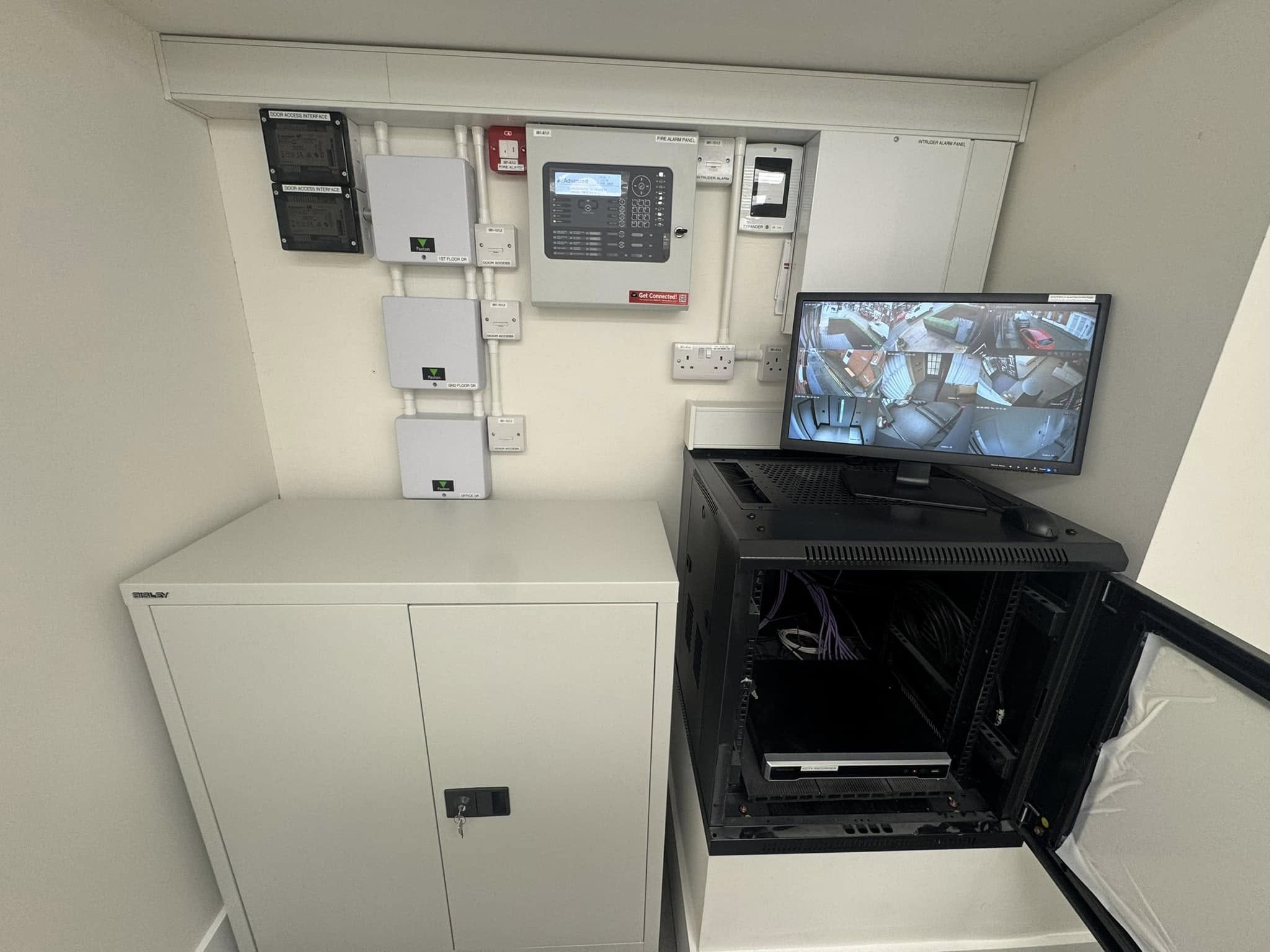 Commercial comms room showing fire alarm panel, CCTV monitor with live feeds, intruder alarm panel and server rack installed by Matrix FSE